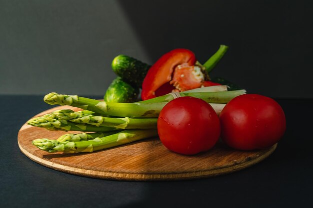 Zdjęcie warzywa leżą na desce pomidory szparagi ogórki czerwona papryka brązowe ciemnoszare tło miejsce na tekst