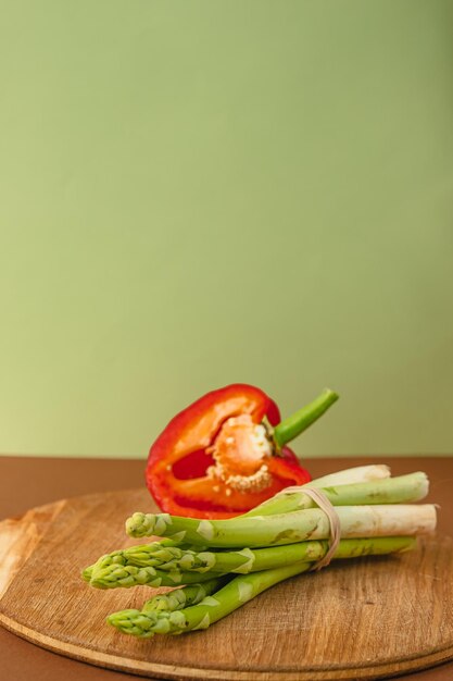 Warzywa leżą na desce szparagi czerwona papryka brązowe jasnozielone tło miejsce na tekst