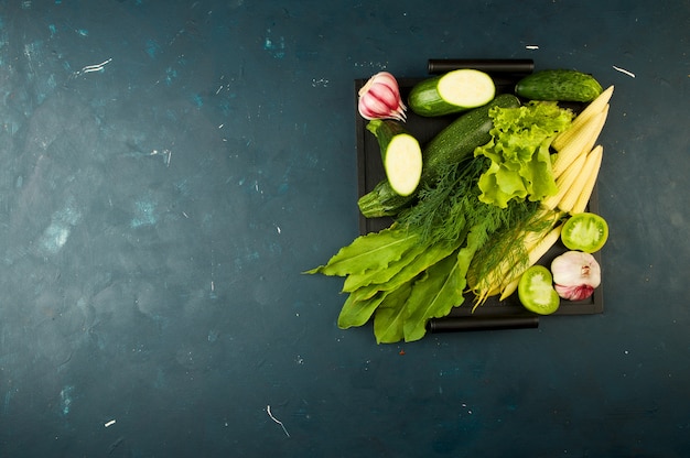 WARZYWA W PUDEŁKU NA KAMIENIU CIEMNY. MŁODE ZIELONE Cebule GARLIC ZUCCHINI JASNE PRZYPRAWY UMIESZCZAJĄ W DREWNIANYM TACU Z RĄCZKAMI NA CIEMNYM TEKSTURZE.