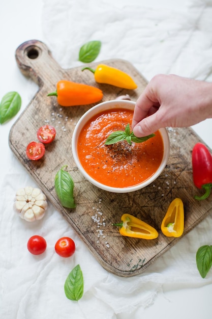 Warzywna wegańska czerwona zupa z pomidorami, papryką, czosnkiem i bazylią Mężczyzna trzyma liść bazylii i wkłada go do zupy