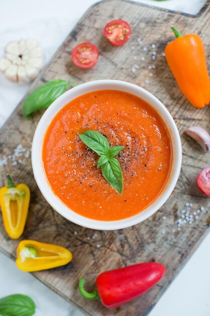 Warzywna wegańska czerwona zupa z pomidorami, papryką, czosnkiem i bazylią na drewnianej desce do krojenia