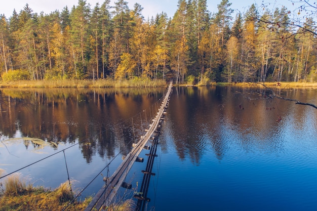 Wąski długi drewniany most wiszący nad jeziorem w Karelii w Rosji. Piękny krajobraz sezonu jesiennego z rzeką i lasem stock photography