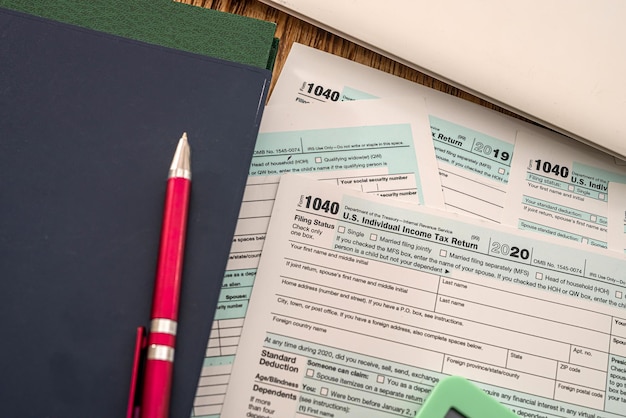 Ważne zamknięte zeszyty, czerwony długopis i formularze podatkowe 1040 leżą na biurku Koncepcja dokumentacji