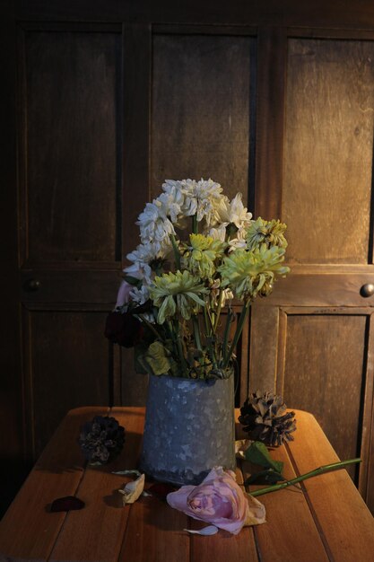 Wazon z kwiatami stoi na stole, a za nim drewniane drzwi.
