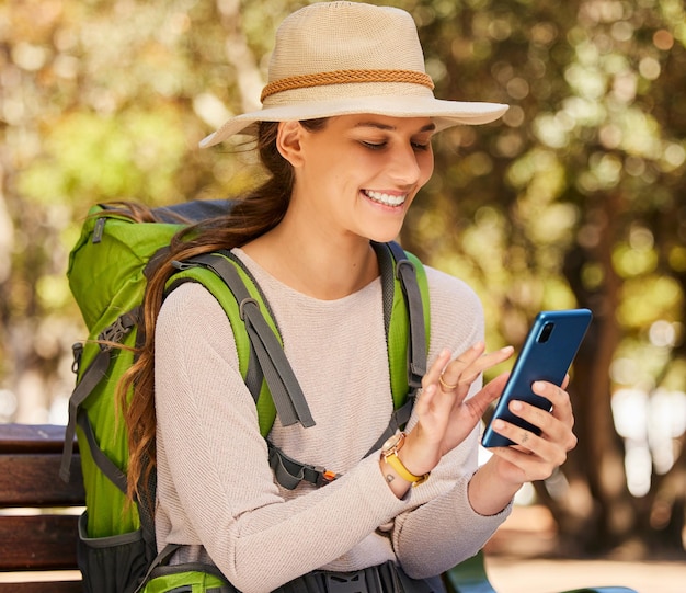 Zdjęcie wędrówka przez telefon i kobieta sprawdzająca gps lub mapę online w lesie szczęśliwy relaks i nawigacja przygoda w przyrodzie i uśmiechnięta kobieta badająca las siedząca, aby wysłać sms-a i przeczytać wiadomość na smartfonie