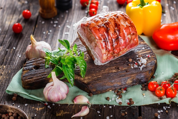 wędzone mięso lub wieprzowina ze smalcem, w plasterkach, pomidorkami koktajlowymi, ziołami i przyprawami, na czarnym drewnianym, krojonym