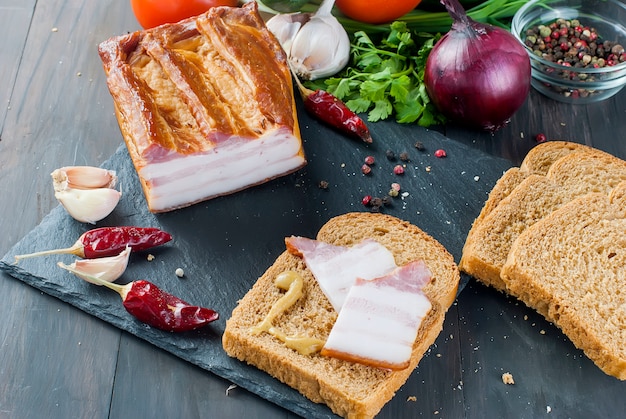 Wędzony boczek z bagietką i warzywami na kamiennej czarnej desce