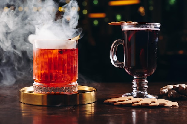 Zdjęcie wędzony staromodny koktajl i grzane wino na stole na ciemnym tle