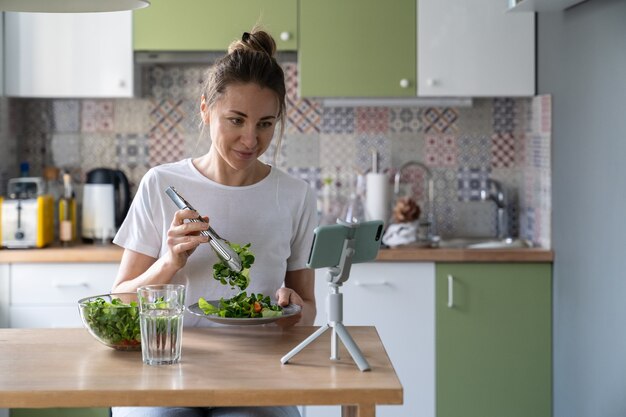 Zdjęcie weganka jedzenie zdrowej sałatki ze świeżych ziół i warzyw oglądając film na smartfonie w domu