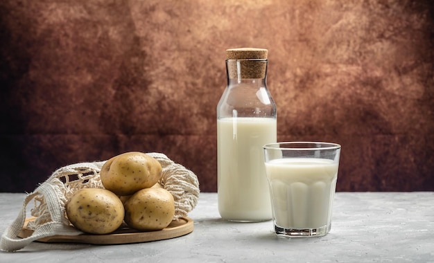 Wegańskie mleko ziemniaczane w szkle i surowe ziemniaki Alternatywne mleko roślinne Trend w zdrowej żywności Zdrowe, czyste odżywianie Dieta wegańska lub bezglutenowa Widok z góry w formacie długiego banera