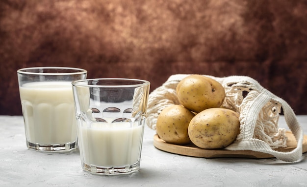 Wegańskie mleko ziemniaczane w szkle i surowych ziemniakach Alternatywna koncepcja superfood na bazie mleka roślinnego Zdrowe, czyste odżywianie Dieta wegańska lub bezglutenowa