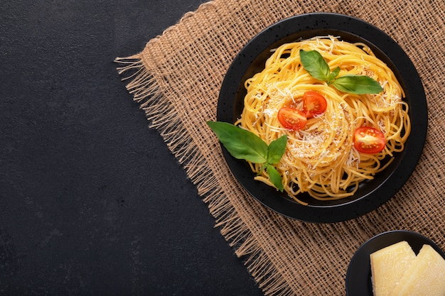 Zdjęcie wegetariański apetyczny klasyczny włoski makaron spaghetti z bazylią, pomidorem i parmezanem na czarnym talerzu na ciemnym stole. widok z góry, poziomy.