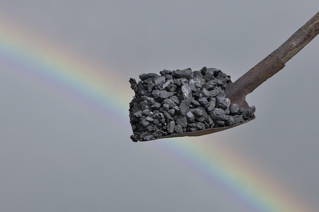 Węgiel kamienny na łopacie na tle nieba i tęczy Kryzys energetyczny