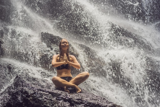 Wellness spa wakacje i koncepcja jogi medytacji Młoda kobieta siedzi w pozycji lotosu na skale w tropikalnym wodospadzie