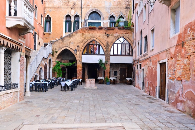 Wenecja, Wenecja Euganejska, Włochy. Stary dziedziniec z małą kawiarnią na świeżym powietrzu. Wąskie puste małe podwórko, stare domy z cegły w Wenecji, Włochy.