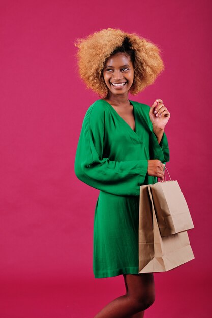 Wesoła afro kobieta trzyma torby na zakupy z brązowego papieru, stojąc nad na białym tle.
