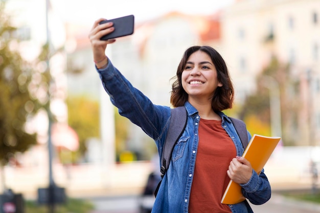 Wesoła arabska studentka biorąca selfie ze smartfonem na zewnątrz