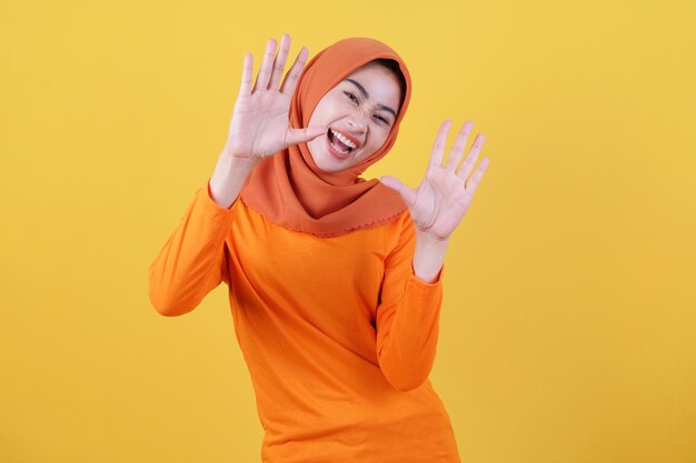 Wesoła atrakcyjna azjatycka kobieta demonstruje miejsce na kopię na pustej żółtej ścianie, ma szczęśliwy przyjazny wyraz, ubrana swobodnie w hidżab, pozuje w pomieszczeniach