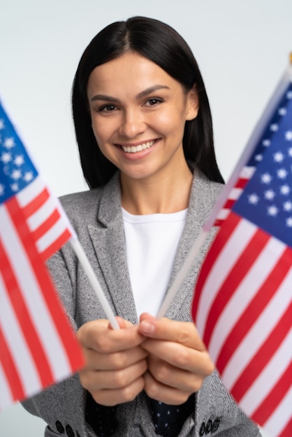 Wesoła Atrakcyjna Kobieta Trzyma Dwie Flagi Usa, Patrząc W Kamerę I Uśmiechając Się Radośnie. Kryty Studio Strzał Na Białym Tle