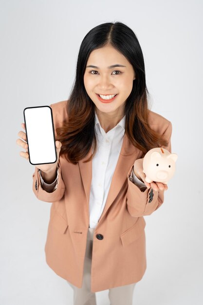 Zdjęcie wesoła azjatycka bizneswoman trzymająca świnię i smartfon odizolowany na białym tle