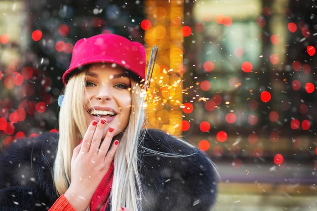 Wesoła blond kobieta zabawy z musujące światła na jarmarku bożonarodzeniowym. Miejsce na tekst