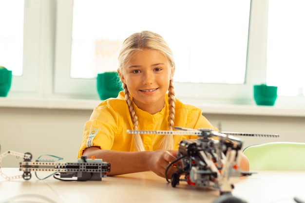 Wesoła blondynka siedzi przy biurku z modelem helikoptera podczas lekcji technologii