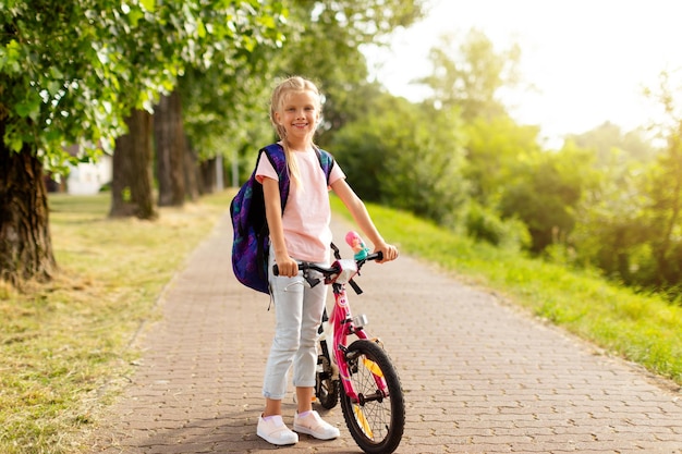 Wesoła dziewczyna przybywająca do szkoły na rowerze w plecaku na początek szkoły stojącej w pobliżu