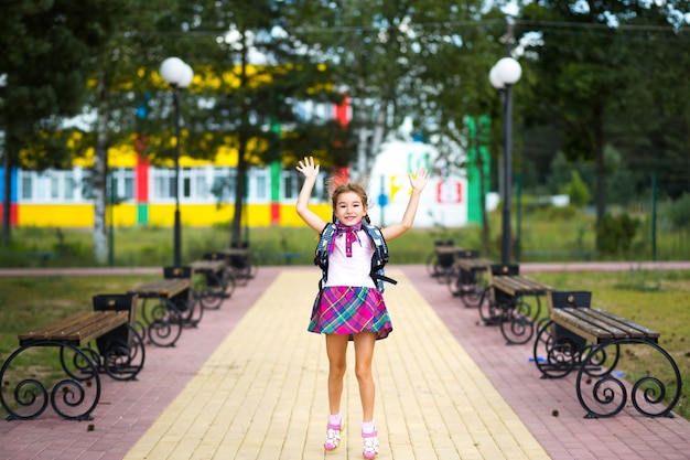 Wesoła dziewczyna z plecakiem iw mundurku szkolnym na dziedzińcu szkolnym. Powrót do szkoły
