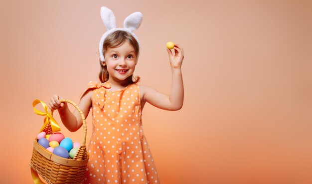 Zdjęcie wesoła dziewczyna z uszami królika na głowie i maską ochronną z koszykiem kolorowych jajek