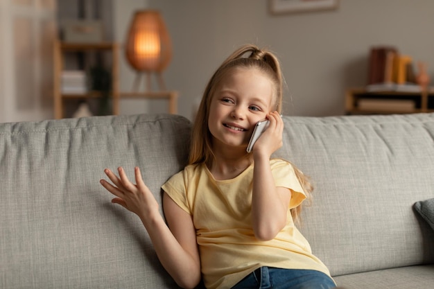 Wesoła dziewczynka rozmawiająca przez telefon komórkowy komunikująca się w domu