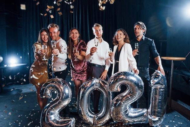 Wesoła grupa ludzi z napojami i balonami w rękach świętujących nowy rok 2021.