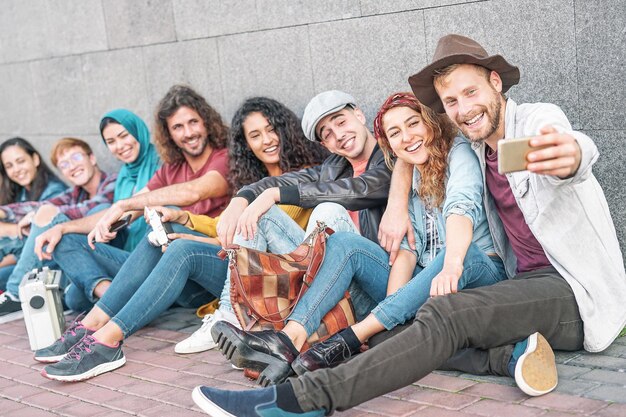 Zdjęcie wesoła grupa przyjaciół robi selfie, siedząc przy ścianie.