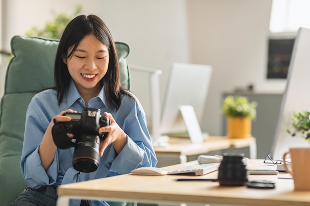 Wesoła japońska dama fotograf trzymająca aparat fotograficzny w miejscu pracy w pomieszczeniu