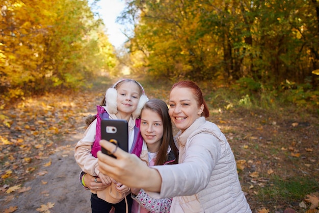 Wesoła kobieta chce zrobić sobie selfie z córkami w jesiennym parku rodzinnych zdjęć szczęśliwych ludzi