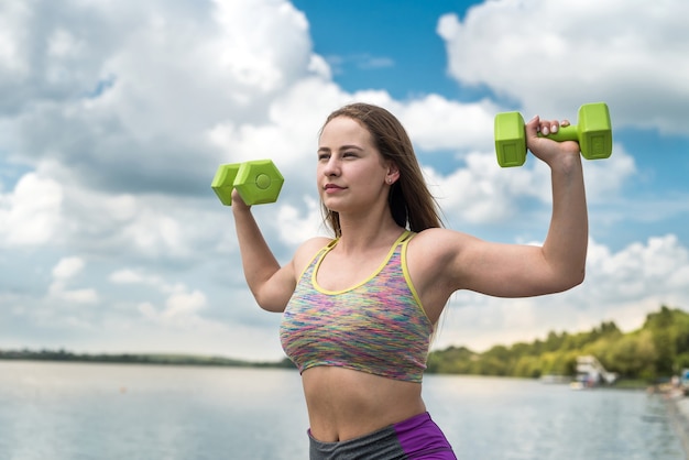 Wesoła kobieta fitness w sprawny ćwiczenia z hantlami, na zewnątrz