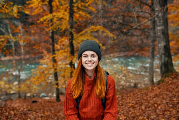 Wesoła kobieta podróżuje w jesiennym lesie w naturze w pobliżu rzeki i wysokich drzew w tle