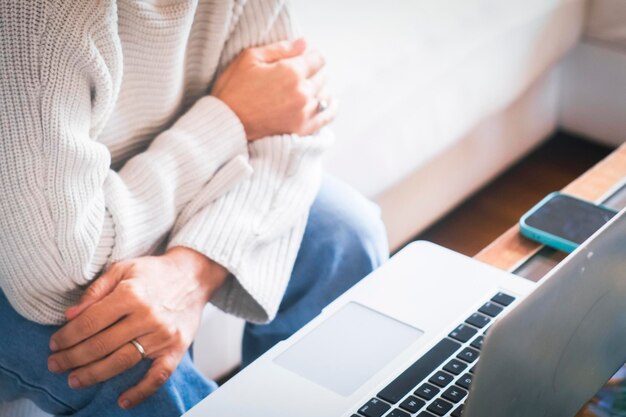 Wesoła kobieta siedzi w swoim przytulnym mieszkaniu i używa laptopa do przeglądania i wyszukiwania w Internecie Młoda kobieta siedzie na kanapie w swoim nowoczesnym mieszkaniem i uśmiecha się do laptopa