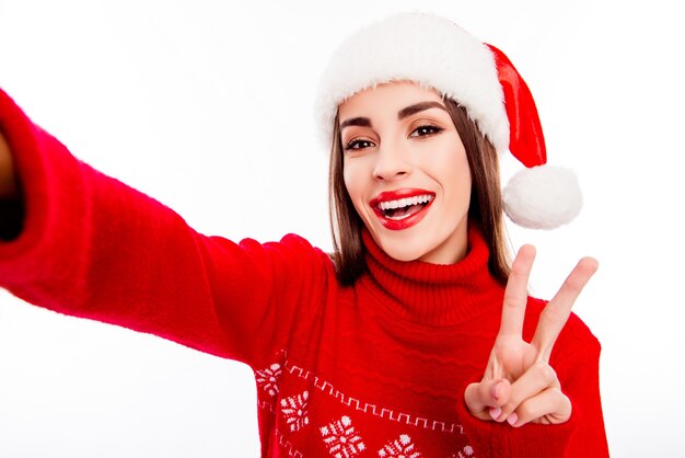 Wesoła kobieta w santa hat robi selfie i gestykuluje znak v