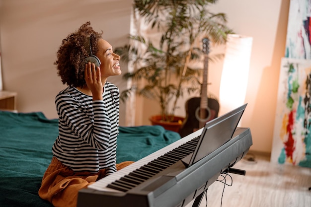Wesoła kobieta w słuchawkach gra na syntezatorze w domu