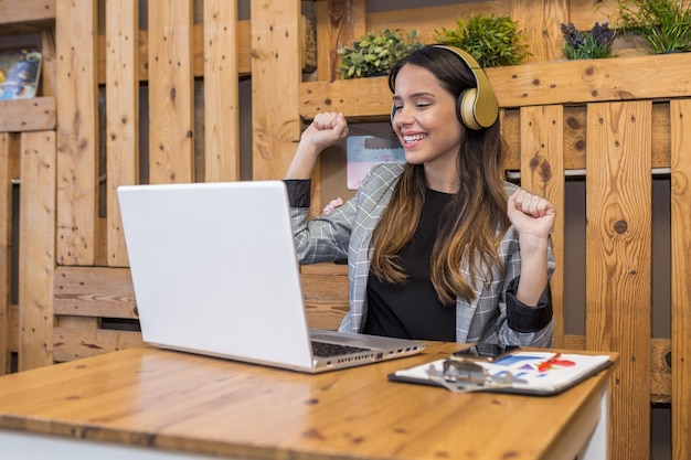 Wesoła kobieta w słuchawkach świętuje sukces w pracy online