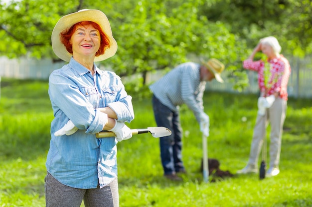 Wesoła kobieta. Wesoła emerytowana kobieta z jasnymi ustami w letnim kapeluszu czuje się szczęśliwa dbając o ogród