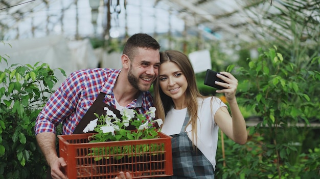 Wesoła, kochająca się para ogrodników, robiąca zdjęcie selfie na aparacie smartfona podczas pracy