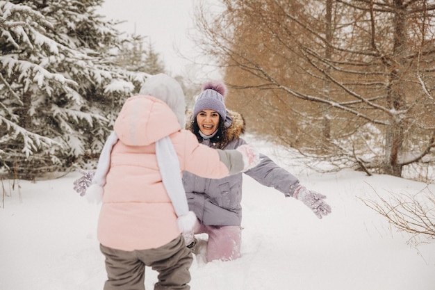 Wesoła mama dogania córkę, która biega przez śnieg w lesie. zimowe spacery