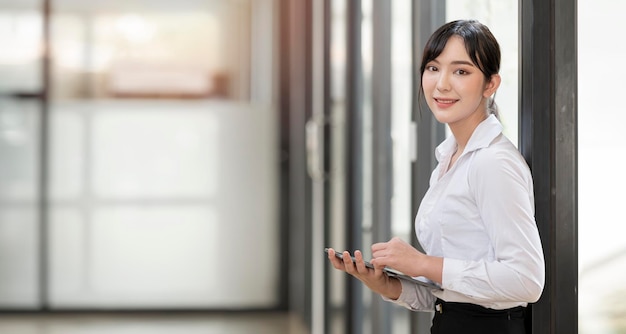 Wesoła młoda azjatycka bizneswoman trzymająca cyfrowy tablet i patrząca na kamerę