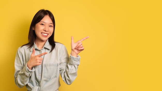 Wesoła młoda azjatycka dama wskazująca na miejsce uśmiechnięta, oferująca miejsce na projekt reklamy na żółto