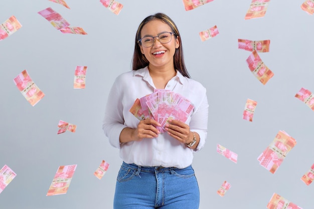 Wesoła młoda Azjatycka kobieta trzymająca banknoty na białym tle nad białym tłem