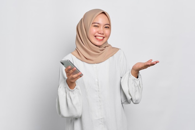 Wesoła młoda azjatycka muzułmanka korzystająca z telefonu komórkowego i świętująca sukces, otrzymując dobre wieści odizolowane na białym tle