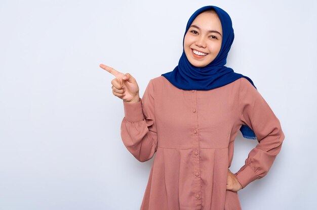 Wesoła Młoda Azjatycka Muzułmańska Kobieta W Różowej Koszuli, Wskazując Palcami Na Miejsce Na Białym Tle Nad Białym Tłem Koncepcja Religijnego Stylu życia Ludzi