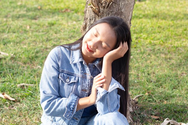 Wesoła młoda dziewczyna siedzi w parku uśmiechając się i nosi kurtkę i dżinsy koncepcji stylu życia