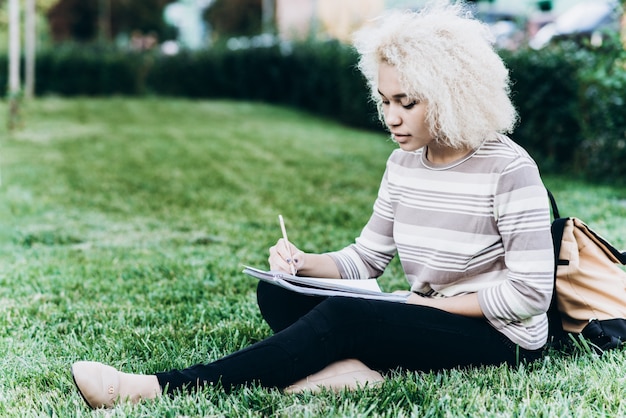 Zdjęcie wesoła młoda dziewczyna student siedzi na trawie w kampusie
